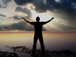 Man standing on a beach and gazing at the sunset with arms wide open